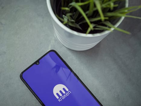 Lod, Israel - July 16,2023: Modern workspace with smartphone with Kraken app launch screen on marble background. Close up top view flat lay.