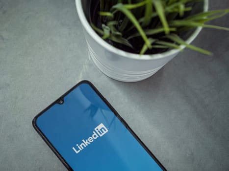 Lod, Israel - July 16,2023: Modern workspace with smartphone with LinkedIn app launch screen on marble background. Close up top view flat lay.