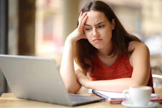 Frustrated student checking content on laptop in a coffee shop terrace