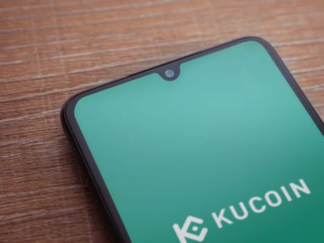 Lod, Israel - July 16,2023: KuCoin app launch screen on smartphone on wooden background. Top view flat lay with copy space.