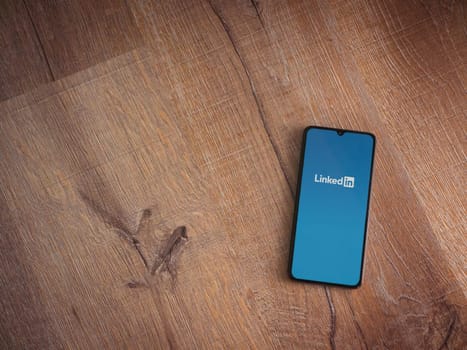 Lod, Israel - July 16,2023: LinkedIn app launch screen on smartphone on wooden background. Top view flat lay with copy space.