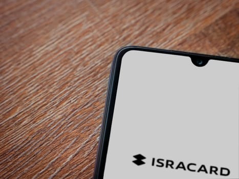 Lod, Israel - July 16,2023: Isracard app launch screen on smartphone on wooden background. Top view flat lay with copy space.