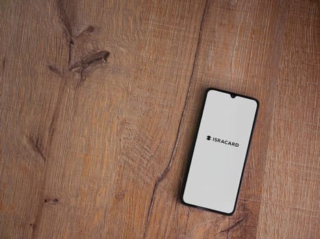 Lod, Israel - July 16,2023: Isracard app launch screen on smartphone on wooden background. Top view flat lay with copy space.