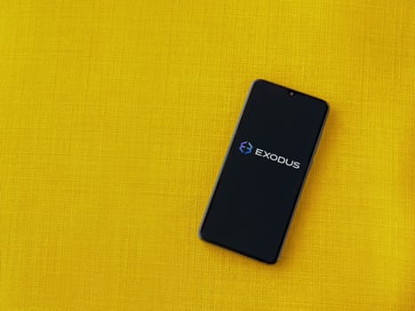 Lod, Israel - July 16,2023: Exodus app launch screen on smartphone on yellow fabric background. Top view flat lay with copy space.