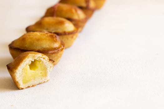 Pasticciotto leccese pastry filled with egg custard cream, typical sweet from Lecce, Italy. Pieces of baked pasticiotto on a white table in a line, apulian breakfast, close up