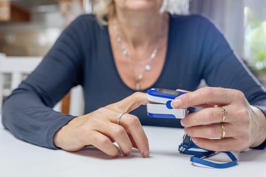Home health prevention. Woman is  measuring pulse  and blood   oxygenation with a compact electronic pulse oximeter at home.