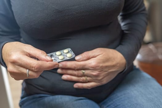 Home treatment concept. Woman holding her aching stomach is ready to use medicine.