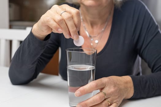 Woman is putting an effervescent vitamin tablet into a glass of water. Horizontally.