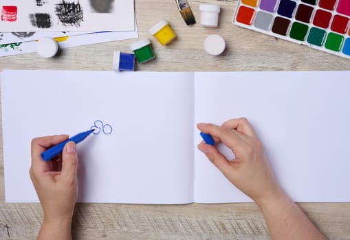 Set of watercolor paints, brushes and paper. Female hands holding a felt-tip pen, top view