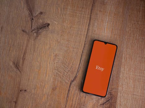 Lod, Israel - July 16,2023: Etsy app launch screen on smartphone on wooden background. Top view flat lay with copy space.
