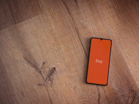 Lod, Israel - July 16,2023: Etsy app launch screen on smartphone on wooden background. Top view flat lay with copy space.
