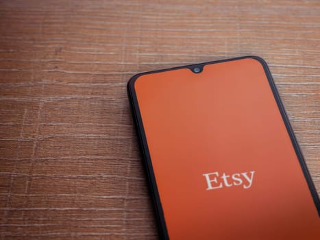 Lod, Israel - July 16,2023: Etsy app launch screen on smartphone on wooden background. Top view flat lay with copy space.