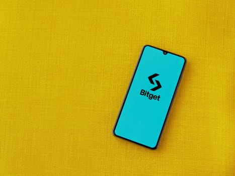 Lod, Israel - July 16,2023: Bitget app launch screen on smartphone on yellow fabric background. Top view flat lay with copy space.