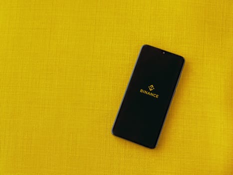 Lod, Israel - July 16,2023: Binance app launch screen on smartphone on yellow fabric background. Top view flat lay with copy space.