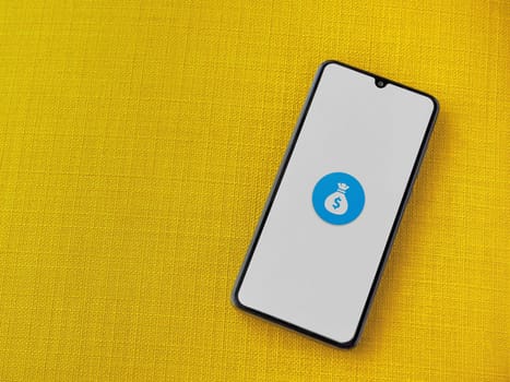 Lod, Israel - July 16,2023: Spender app launch screen on smartphone on yellow fabric background. Top view flat lay with copy space.
