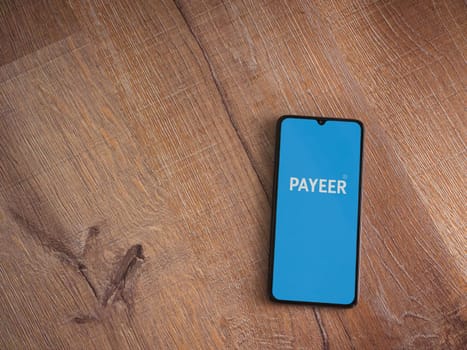 Lod, Israel - July 16,2023: PAYEER app launch screen on smartphone on wooden background. Top view flat lay with copy space.