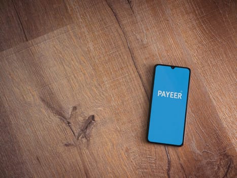 Lod, Israel - July 16,2023: PAYEER app launch screen on smartphone on wooden background. Top view flat lay with copy space.