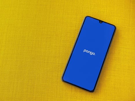 Lod, Israel - July 16,2023: Pango app launch screen on smartphone on yellow fabric background. Top view flat lay with copy space.