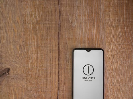 Lod, Israel - July 16,2023: One Zero app launch screen on smartphone on wooden background. Top view flat lay with copy space.