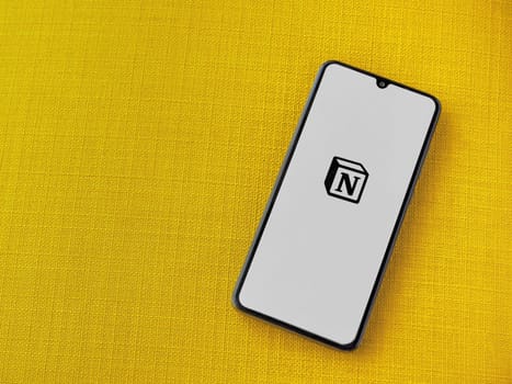 Lod, Israel - July 16,2023: Notion app launch screen on smartphone on yellow fabric background. Top view flat lay with copy space.