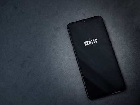 Lod, Israel - July 16,2023: OKX app launch screen on smartphone on dark marble stone background. Top view flat lay with copy space.
