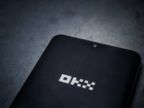 Lod, Israel - July 16,2023: OKX app launch screen on smartphone on dark marble stone background. Top view flat lay with copy space.