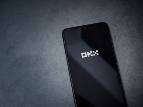 Lod, Israel - July 16,2023: OKX app launch screen on smartphone on dark marble stone background. Top view flat lay with copy space.
