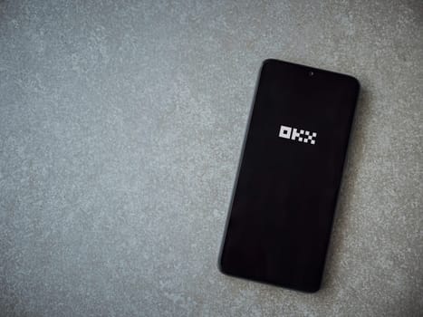 Lod, Israel - July 16,2023: OKX app launch screen on smartphone on ceramic stone background. Top view flat lay with copy space.