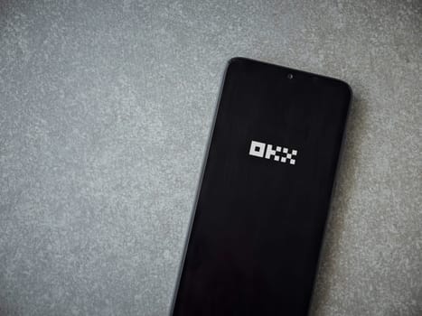Lod, Israel - July 16,2023: OKX app launch screen on smartphone on ceramic stone background. Top view flat lay with copy space.