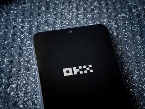 Lod, Israel - July 16,2023: OKX app launch screen on smartphone on metallic background. Close up top view flat lay.