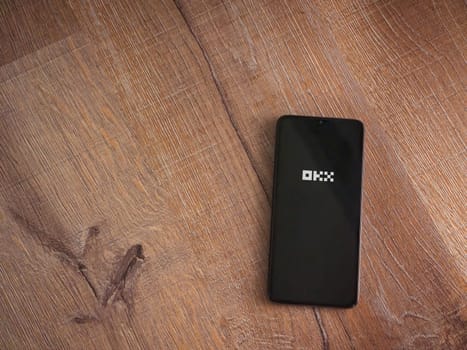 Lod, Israel - July 16,2023: OKX app launch screen on smartphone on wooden background. Top view flat lay with copy space.
