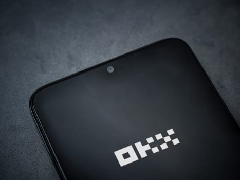Lod, Israel - July 16,2023: OKX app launch screen on smartphone on dark marble stone background. Top view flat lay with copy space.