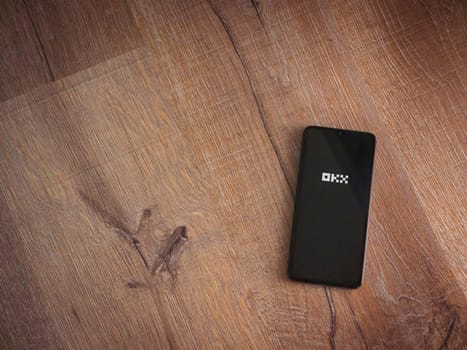 Lod, Israel - July 16,2023: OKX app launch screen on smartphone on wooden background. Top view flat lay with copy space.