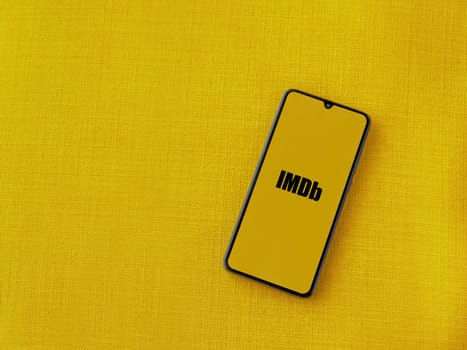 Lod, Israel - July 16,2023: IDMb app launch screen on smartphone on yellow fabric background. Top view flat lay with copy space.