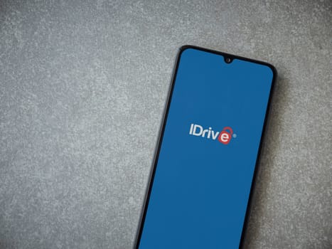 Lod, Israel - July 16,2023: IDrive Online Backup app launch screen on smartphone on ceramic stone background. Top view flat lay with copy space.