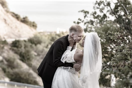 Happy newlyweds kiss against the backdrop of a beautiful mountain landscape, sepia