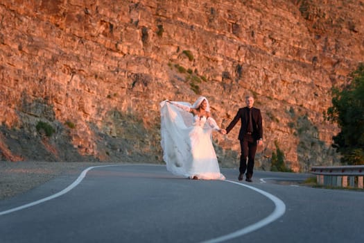 Happy newlyweds running along a mountain asphalt road