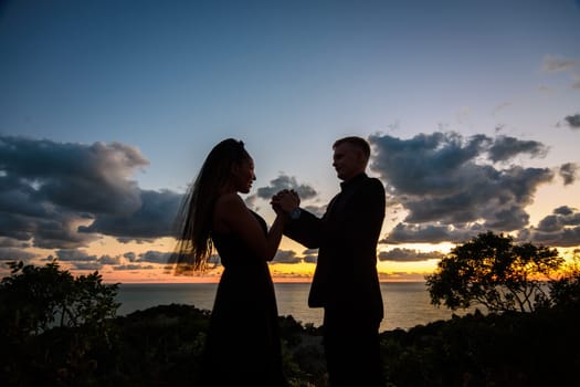 Happy young couple holding each other's hands in backlight against sunset background
