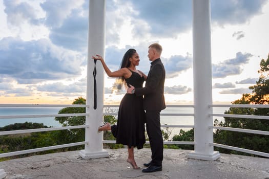 A young couple in a gazebo against the backdrop of a beautiful landscape, the girl holds the guy's tie