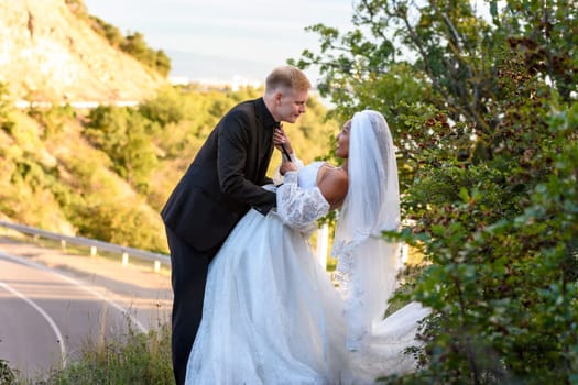 Happy newlyweds kiss against the backdrop of a beautiful mountain landscape, the girl holds the guy by the tie