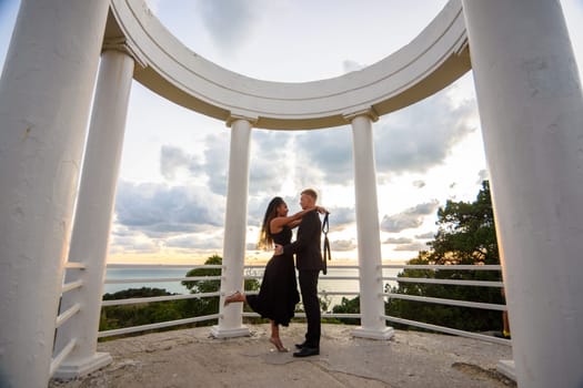 A young couple hugs in a gazebo against the backdrop of a beautiful landscape