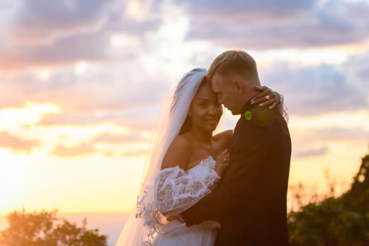 Happy newlyweds hugging against the background of a backlit sunset