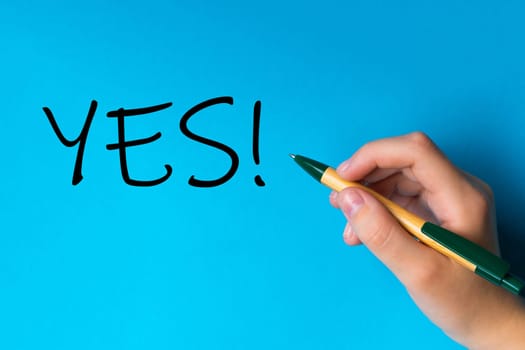 Children hand with pen write on a blue white background. Writing hand. Word YES