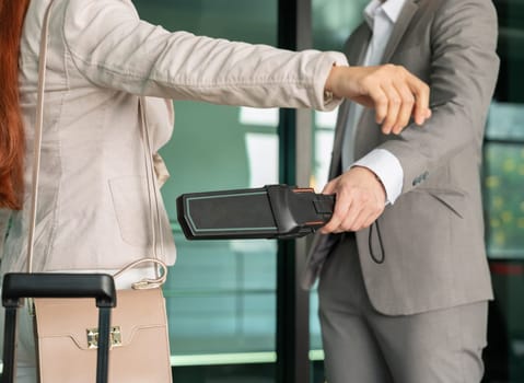 Security male officer using metal detector on female passenger at airport boarding gate. Airport travel and security concept.
