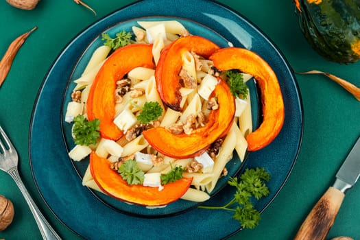 Pasta with baked pumpkins and nuts in a ceramic plate. Tasty autumn food. Top view.
