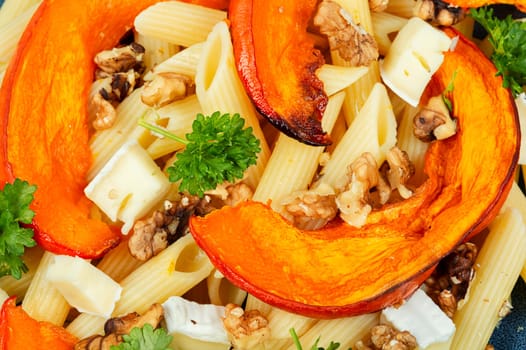 Pasta with baked pumpkins and nuts in a ceramic plate. Tasty autumn food. Top view.