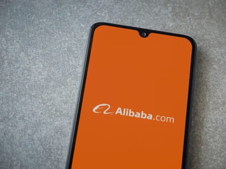 Lod, Israel - July 16,2023: Alibaba.com app launch screen on smartphone on ceramic stone background. Top view flat lay with copy space.