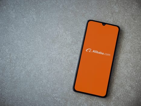 Lod, Israel - July 16,2023: Alibaba.com app launch screen on smartphone on ceramic stone background. Top view flat lay with copy space.