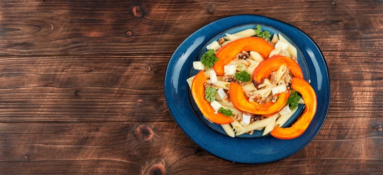 Pasta with baked pumpkins and nuts in a ceramic plate. Tasty autumn food. Top view.
