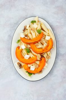 Pasta with baked pumpkins and nuts in a ceramic plate. Tasty autumn food. Top view.